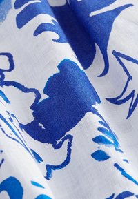 Blå och vit mönstrad tyg, med abstrakta former och flytande linjer. Materialet verkar lätt och texturerat, idealiskt för kläder.