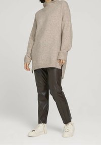 Oversized beige tröja med ribbad nederkant och muddar, kombinerad med åtsittande bruna läderbyxor och vita hög-top sneakers.