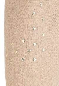 Tela texturada de color rosa claro con pequeños remaches metálicos en forma de corazón esparcidos por la superficie. Sensación suave, diseño casual.