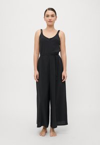 Mono negro con tirantes finos, escote en V, cinturón atado en la cintura, piernas anchas y textura suave, presentado sobre un fondo neutro.