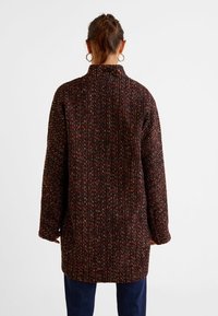 Abrigo de mezcla de lana con un patrón multicolor texturizado, cuello alto, silueta oversize y mangas largas. La vista trasera muestra un detalle mínimo.