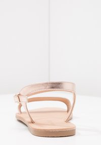 Vaaleanpunakulta tasapohjaiset sandalsit, joissa on kaksi nilkkahihnaa, synteettinen päällinen ja litteä pohja. Sileä pinta, minimalistinen muotoilu, säädettävä solkipitsi.