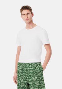 T-shirt bianco a maniche corte con scollatura rotonda, abbinato a pantaloni verdi a fantasia con un design di foglie. Texture di cotone liscia.