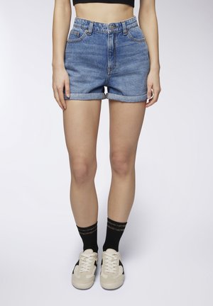 Shorts in denim con vita alta, con risvolti e lavaggio azzurro chiaro. Abbinati a sneakers bianche e calze nere con una striscia dorata.