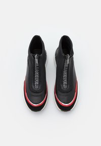 Para czarnych sneakersów z zamkiem błyskawicznym, z czerwonymi i białymi akcentami oraz napisem "KARL LAGERFELD" na klapie zamka, widziana z góry.