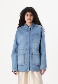 Denimjakke i lys blå med krage, fire frontlommer, lange ermer og avslappet passform. Glatt tekstur og uformelt design.
