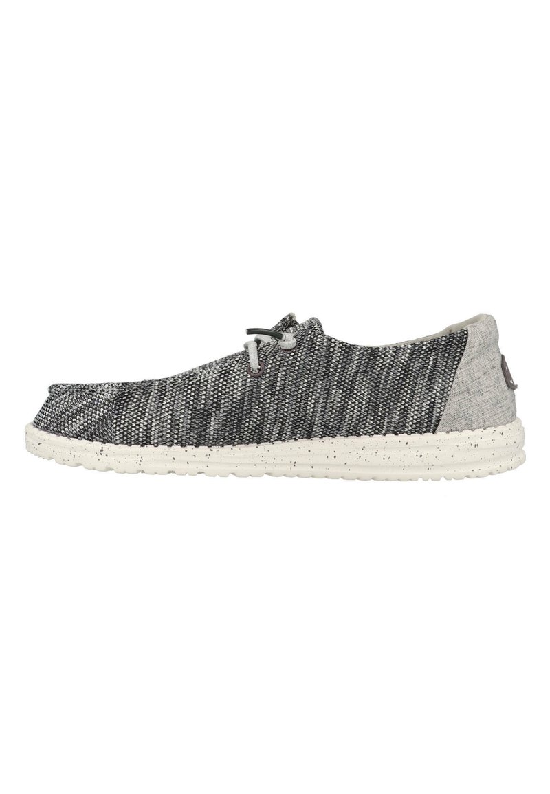 Zapato textil gris con un patrón tejido, puntera redondeada y suela moteada blanca. Presenta un sistema de cierre con cordones y un tacón texturizado en contraste.