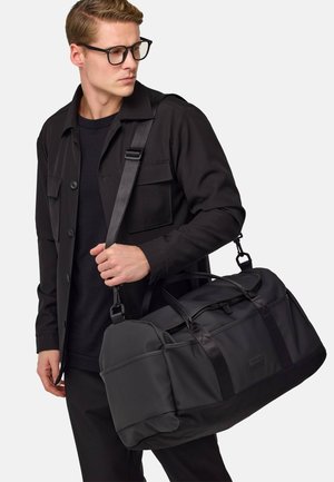 Black duffel bag with a smooth texture, featuring dual handles and a detachable shoulder strap. Includes zip closure and front pocket.