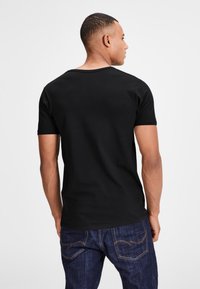 Schwarzes T-Shirt mit kurzen Ärmeln aus Baumwolle, mit einem runden Ausschnitt und glatter Textur, kombiniert mit dunkelblauen Jeans.