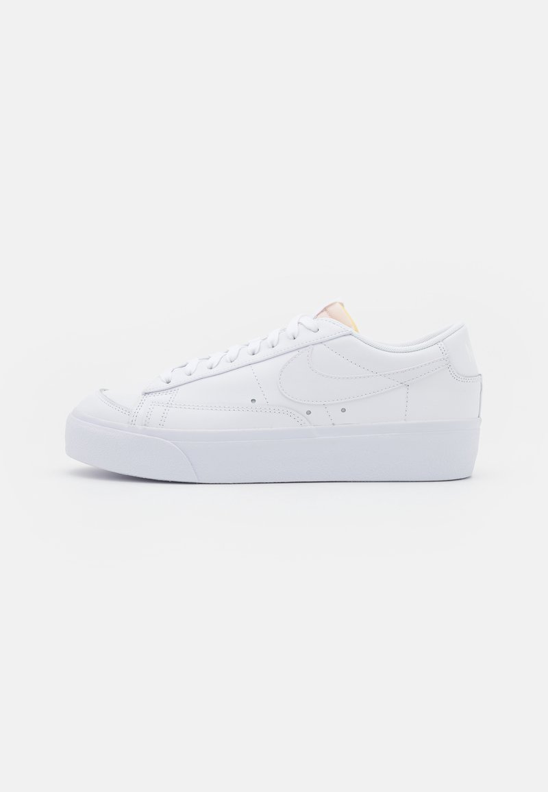 Baskets basses en cuir blanc avec des lacets blancs, une semelle épaisse et un logo swoosh cousu sur le côté.