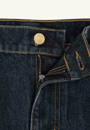 Jeans di jeans blu scuro con cerniera metallica parzialmente aperta e chiusura con bottone in ottone che mostra cuciture dettagliate.