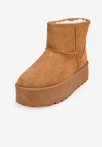 Stivale alla caviglia in suede beige con punta rotonda, fodera morbida e suola spessa. Presenta cuciture evidenti e una texture superiore morbida.