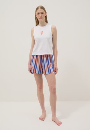 Young woman wearing white sleeveless top with small lobster graphic and blue, orange, and white striped shorts, standing barefoot.