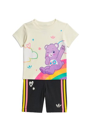 Cremefarvet kortærmet top med lilla bjørn på en regnbue, kombineret med sorte shorts med lyserøde og gule striber samt hvide hjerte- og stjernedesign.