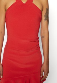 Vestido ajustado vermelho com decote halter, detalhes franzidos laterais e bainha rodada. Feito de tecido texturizado, apresentando um acabamento suave.