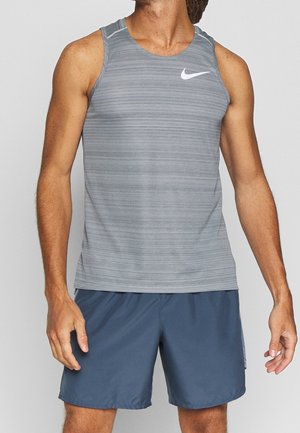 Grey striped athletic tank top with a round neckline and white Nike logo. Paired with blue shorts, showcasing a lightweight, breathable fabric.