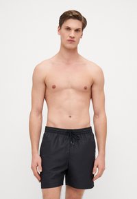 Pantaloni da nuoto neri realizzati in tessuto leggero, con una vita elasticizzata con cordino, tasche laterali e una vestibilità comoda.