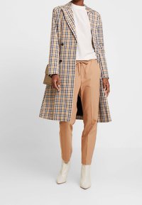 Kollad lång kappa i gult, marinblått och vitt, kombinerad med beige dragkedjebyxor och vita ankelstövlar. Slät textur och skräddarsydd passform.