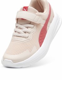 Zapatilla de malla rosa claro con suela blanca y acentos rojos. Presenta una sola correa y cordones con un panel texturizado en el lateral.