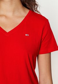 Maglietta in cotone rossa con scollatura a V e maniche corte. Presenta un piccolo logo ricamato sulla parte superiore sinistra del petto. Tessuto liscio.