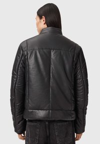 Sort læderjakke med krave, polstret design og synlige sømme. Har en cropped længde og skrå skuldersyning.