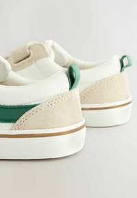Zapatillas blancas con acentos en verde y beige, que presentan un diseño texturizado y una lengüeta en el talón para facilitar su puesta.