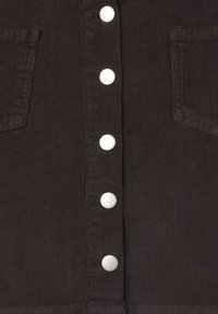 Vestito in velluto a coste marrone scuro con bottoni a pressione argentati, dotato di due tasche sul petto e una superficie testurizzata.