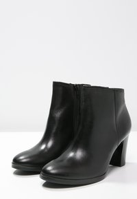 Une paire de bottines en cuir noir avec des fermetures éclair latérales et des talons en bloc, présentées sur une surface blanche.