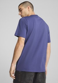 Violet medvilninė t-shirt su trumpomis rankovėmis ir apvalia iškirpte. Turi paprastą dizainą ir laisvą fasoną, rodomas šoninėje ir užpakalinėje pusėje.