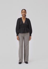 Black peplum top with puffed sleeves and a V-neck; paired with light gray straight-leg trousers and black slip-on shoes. Neutral background.