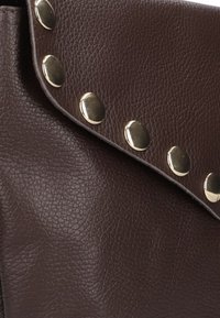 Bruine, gestructureerde leren handtas met een klepopening, voorzien van grote metalen studs langs de rand als accent.