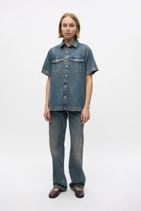 Denim short-sleeve shirt with button closure, two chest pockets, faded blue color, paired with light blue straight-leg jeans and dark loafers.