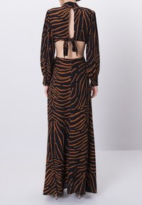 Maxime dress with a black base and brown tiger stripe pattern, featuring long sleeves, a keyhole back, and a tied neck closure.