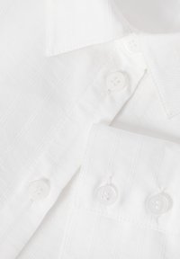 Chemise blanche à rayures verticales, col pointu et boutons ronds blancs. Texture lisse avec des détails de couture subtils.