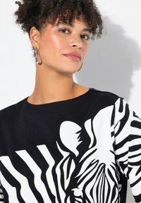 Top bianco e nero con un audace design a stampa zebra, realizzato in tessuto morbido. Collo tondo e maniche corte con una vestibilità rilassata.