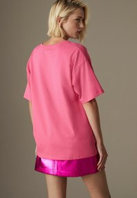 Overdimensioneret lyserød bomulds t-shirt med korte ærmer, glat tekstur og afslappet pasform, parret med en skinnende metallisk lyserød miniskirt.