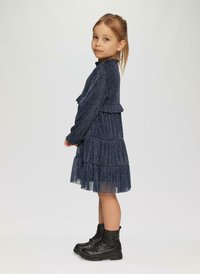Robe bleu marine avec un col à volants, des manches longues et une jupe en tulle superposée. Associée à des bottines noires à lacets.