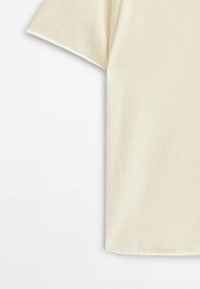 T-shirt en coton à manches courtes de couleur crème, présenté de la moitié de la manche jusqu'à l'ourlet inférieur sur fond blanc.