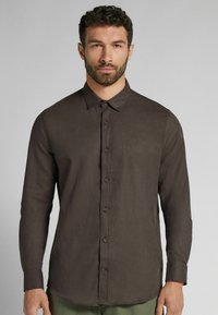 Bruine lange mouwen shirt met een button-down kraag, gemaakt van textuurstof. Heeft knopen aan de voorkant en een zoom die aan de zijkanten omhoog krult.