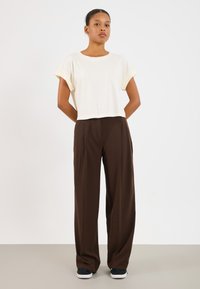 Camiseta branca cortada com mangas enroladas, combinada com calças largas castanhas. As calças têm uma textura suave e ligeiras pregas. Ténis pretos.