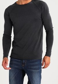 Maglietta a maniche lunghe grigia scura in tessuto testurizzato, con collo tondo e maniche raglan, abbinata a jeans in denim blu.