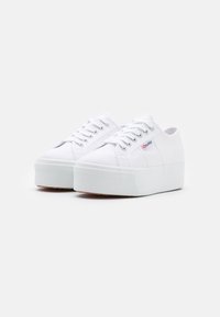 Sneakers bianchi in tela con suola platform spessa, caratterizzati da punta tonda, chiusura con lacci e discreto logo del brand sul lato. Suola testurizzata.