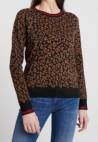 Bruine en zwarte gebreide trui met een gevlekte print, kraag met rode accenten en zwarte geribbelde manchetten. Soepele textuur, klassieke pasvorm.