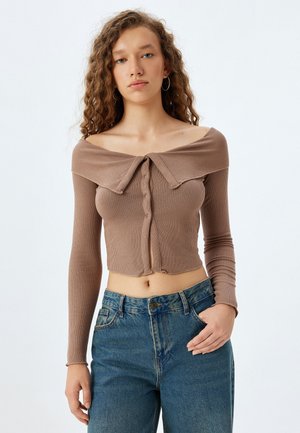 Brun ribbet crop top med en bred off-shoulder krave, knaplukning og lange ærmer, parret med højtaljede blå jeans.