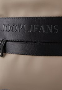 Borsa beige con una banda nera texturizzata e il logo in rilievo "JOOP! JEANS" e chiusura con zip nera nella parte superiore.