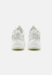 Witte sneakers met vlinderaccenten op de hiel, gestructureerd materiaal, ronde vorm en verhoogd logo-detail op de zijkant.