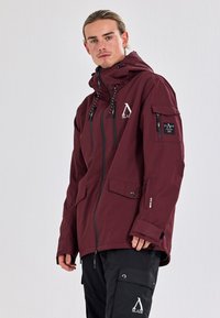 Maroon waterproof jacket with a front zipper, adjustable hood, and multiple pockets. Features logo detail and drawstring accents.