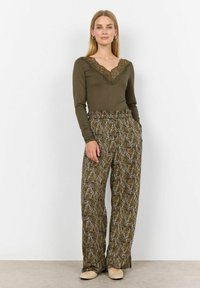 Olijfgroen langetermijnsleeve top met een kanten V-hals, gecombineerd met loszittende, gestreepte broeken in aardetinten met abstracte ontwerpen.
