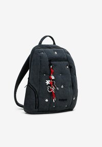 Zwarte rugzak van textuurstof met een doorgestikt ontwerp. Voorzien van rode accenten, meerdere met rits afgesloten vakken en decoratieve bedeltjes.