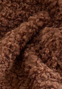 Tissu texturé et duveteux de couleur brune riche, avec des fibres enroulées serrées créant une apparence douce et chaude, offrant une sensation de confort.